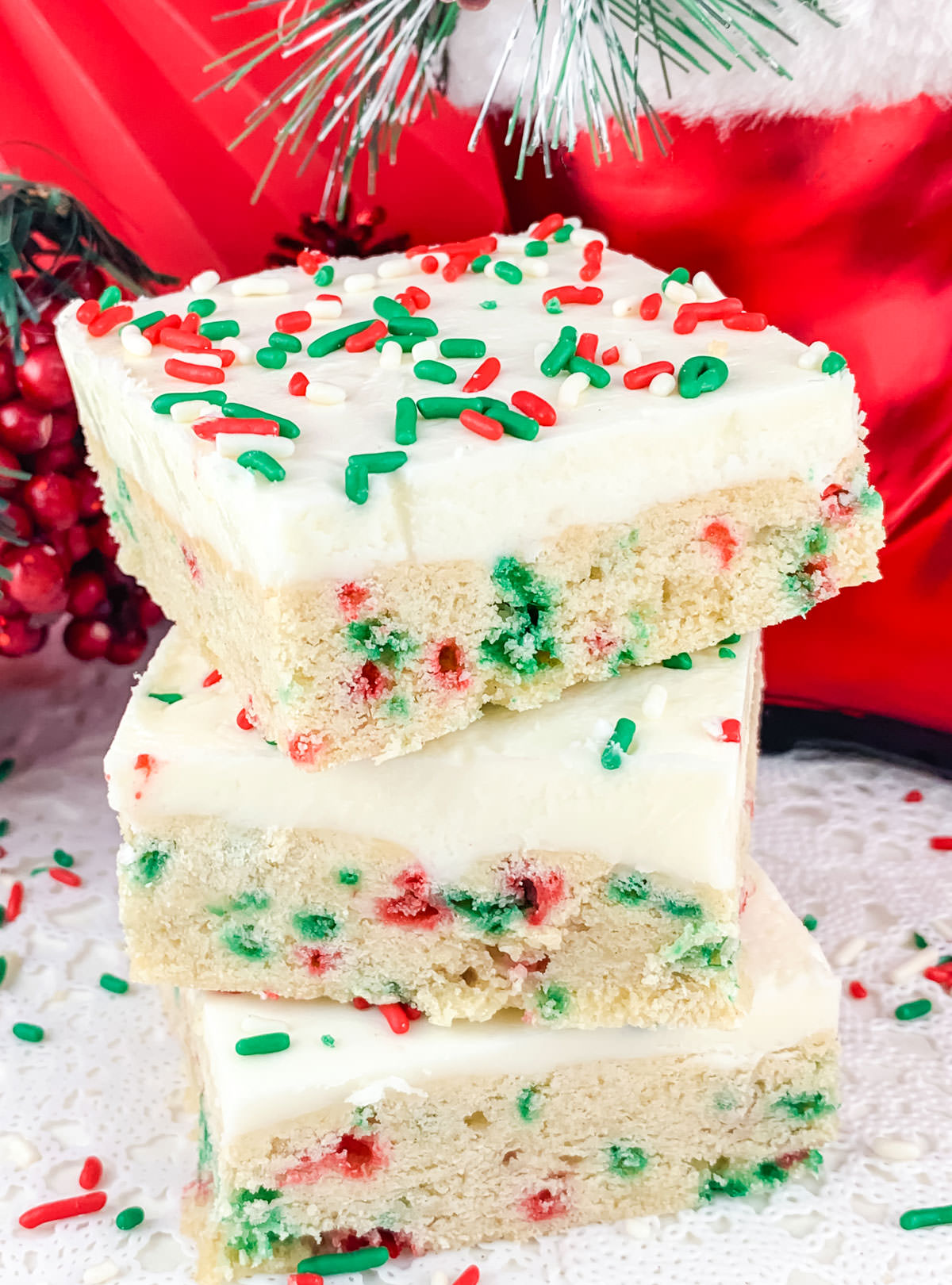 Closeup on a stack of three Peppermint Sugar Cookie Bars sitting on a white table surrounded by red white and green sprinkles.