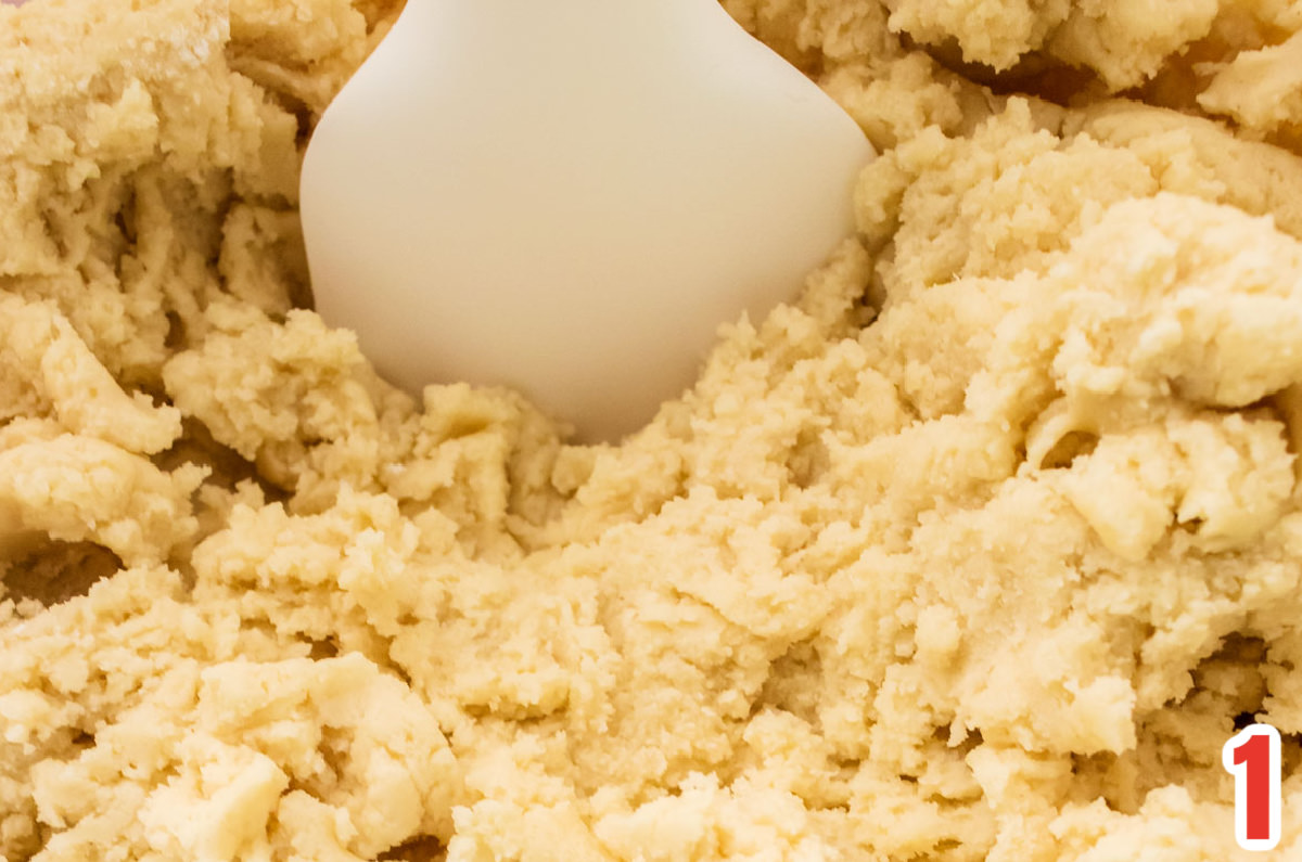 Closeup on a batch of sugar cookie dough and a wooden spatula.