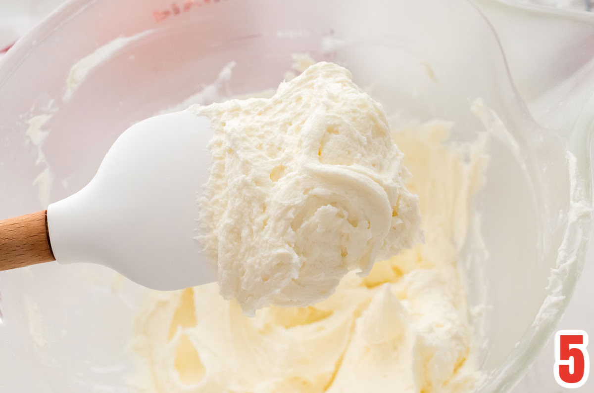 Closeup on a glass mixing bowl filled with Peppermint Buttercream Frosting and a white spatula.