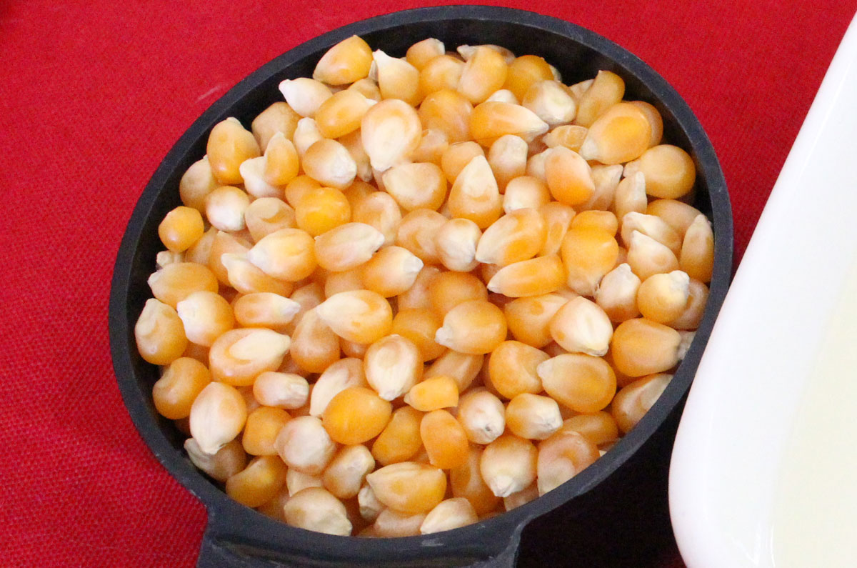 Closeup on a measuring cup filled with popcorn kernels sitting on a red tablecloth.