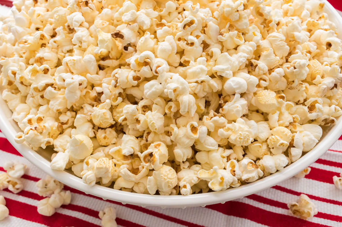 Closeup of a large white serving dish filled with homemade popcorn that is spilling out onto a red and white kitchen towel.