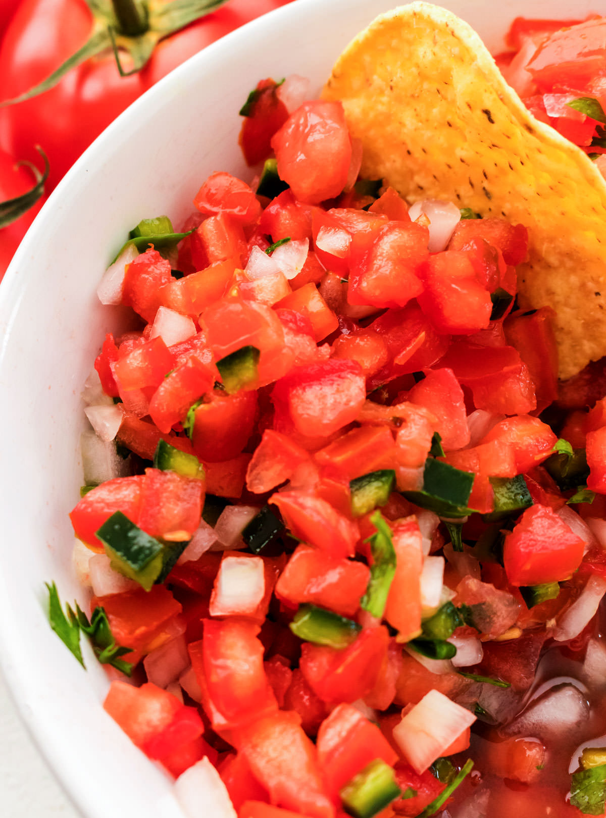 Closeup on a white bowl filled with Pico de Gallo and a single tortilla chip.