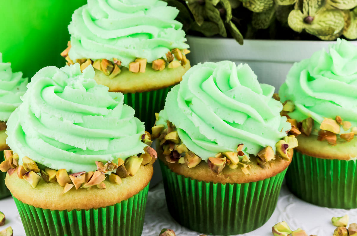 Four Pistachio Cupcakes with Pistachio Whipped Cream Frosting sitting on a white table.