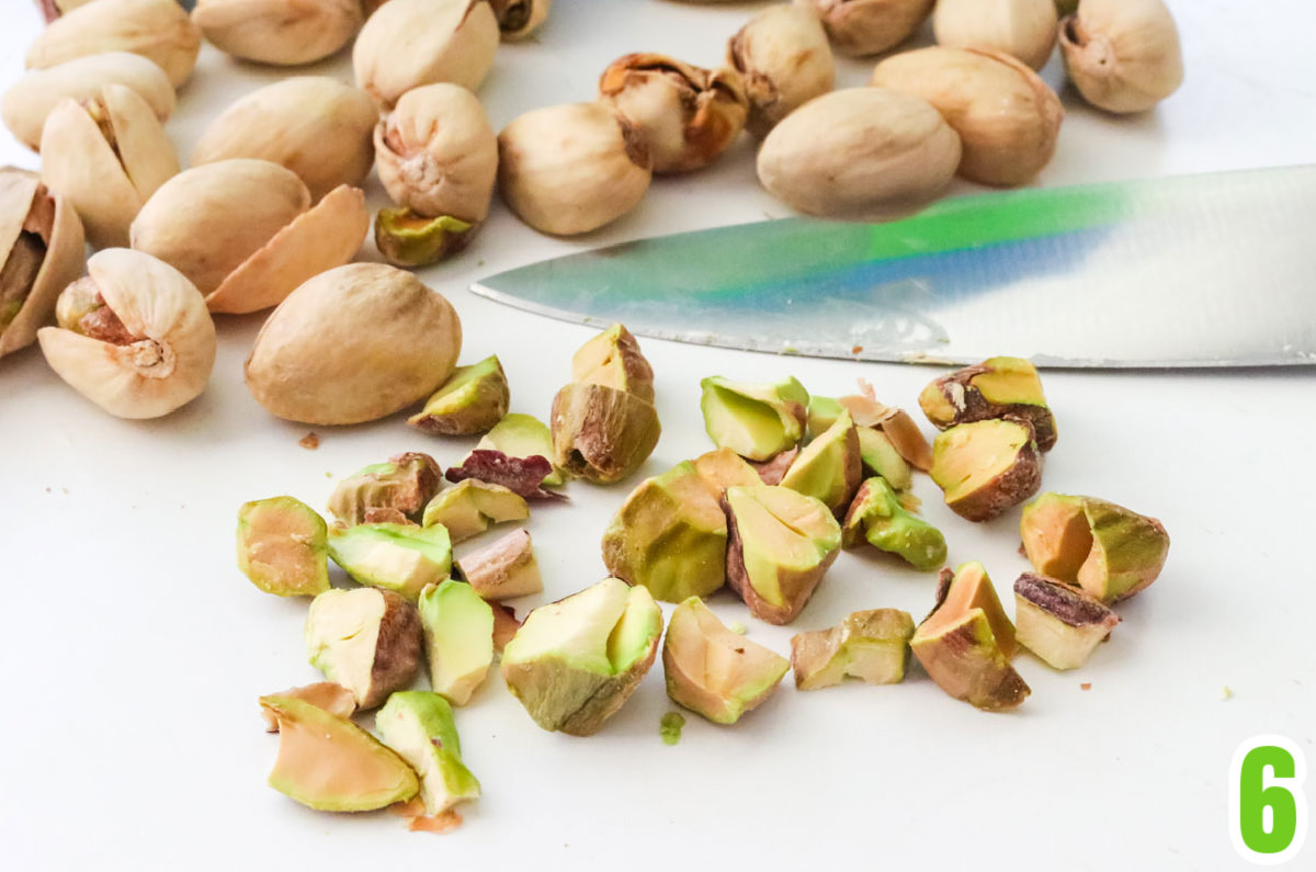 Raw pistachios, some shelled some not shelled, laying on a white table.