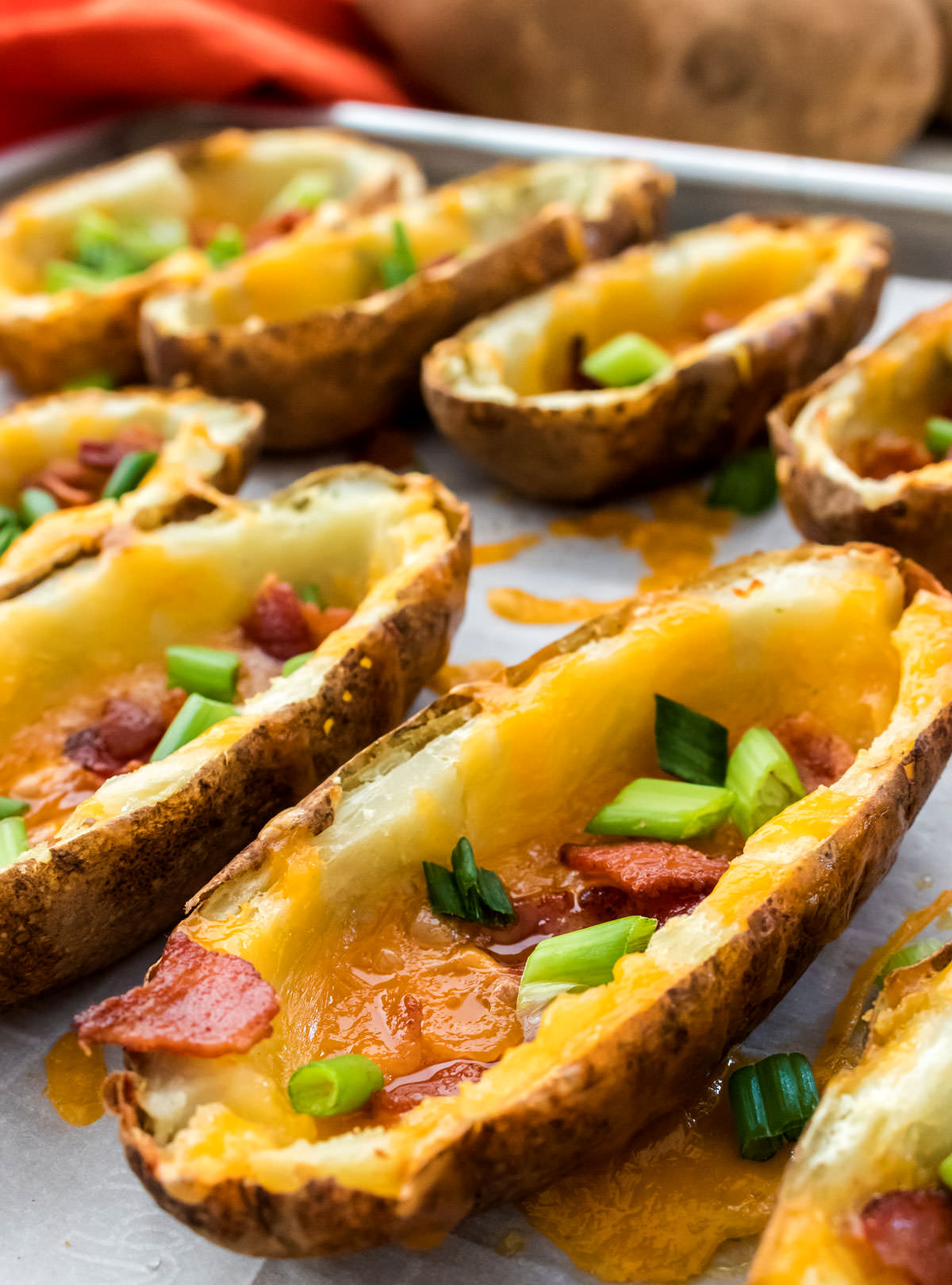 Closeup on eight Potato Skins just out of the oven sitting on a cookie sheet covered in parchment paper.