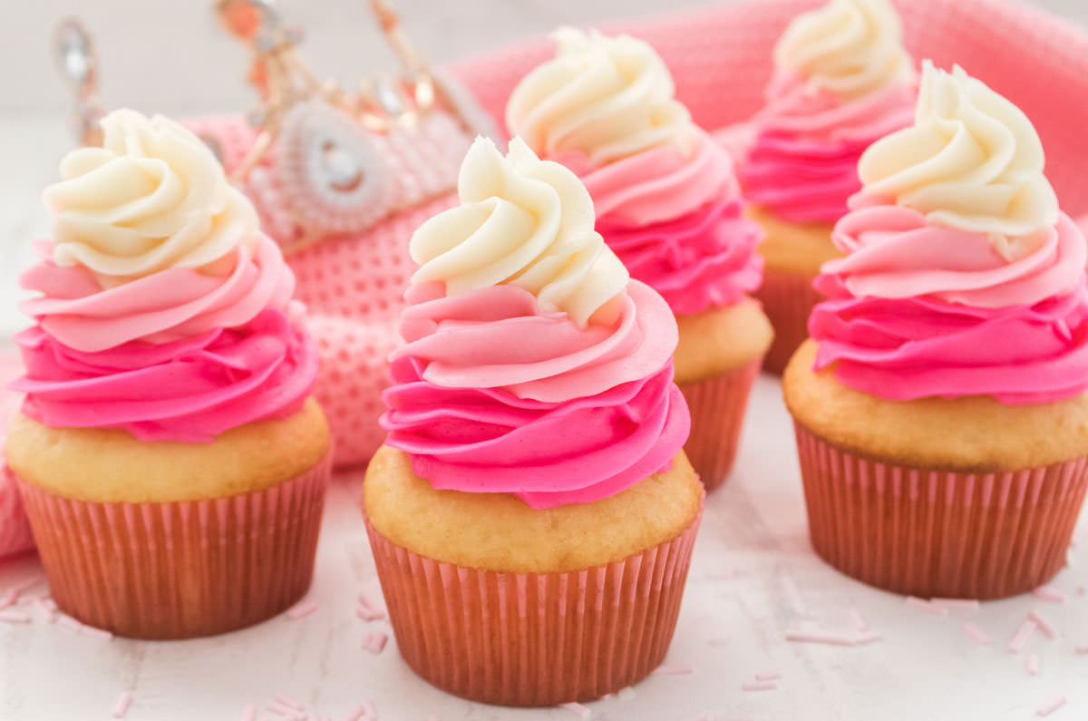 Closeup on five Pink Ombre Princess Cupcakes sitting on a white table in front of a pink table linen and a pink princess tiara.