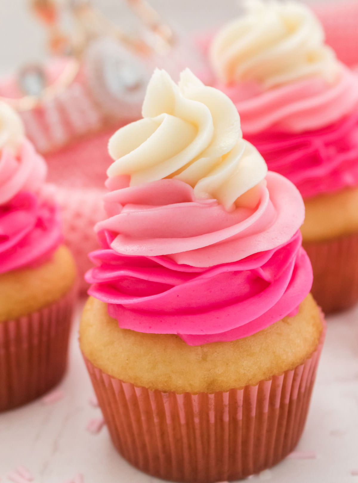 Close of three Princess Cupcakes sitting on a white table in front of a pink towel and a pink princess tiara.