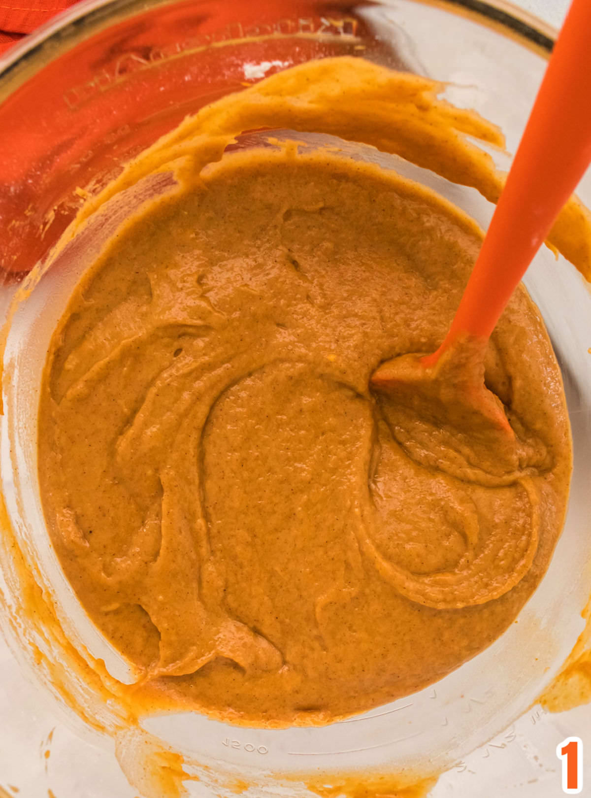 Closeup on a bowl of Pumpkin Bar batter in a glass bowl with a orange spoon.