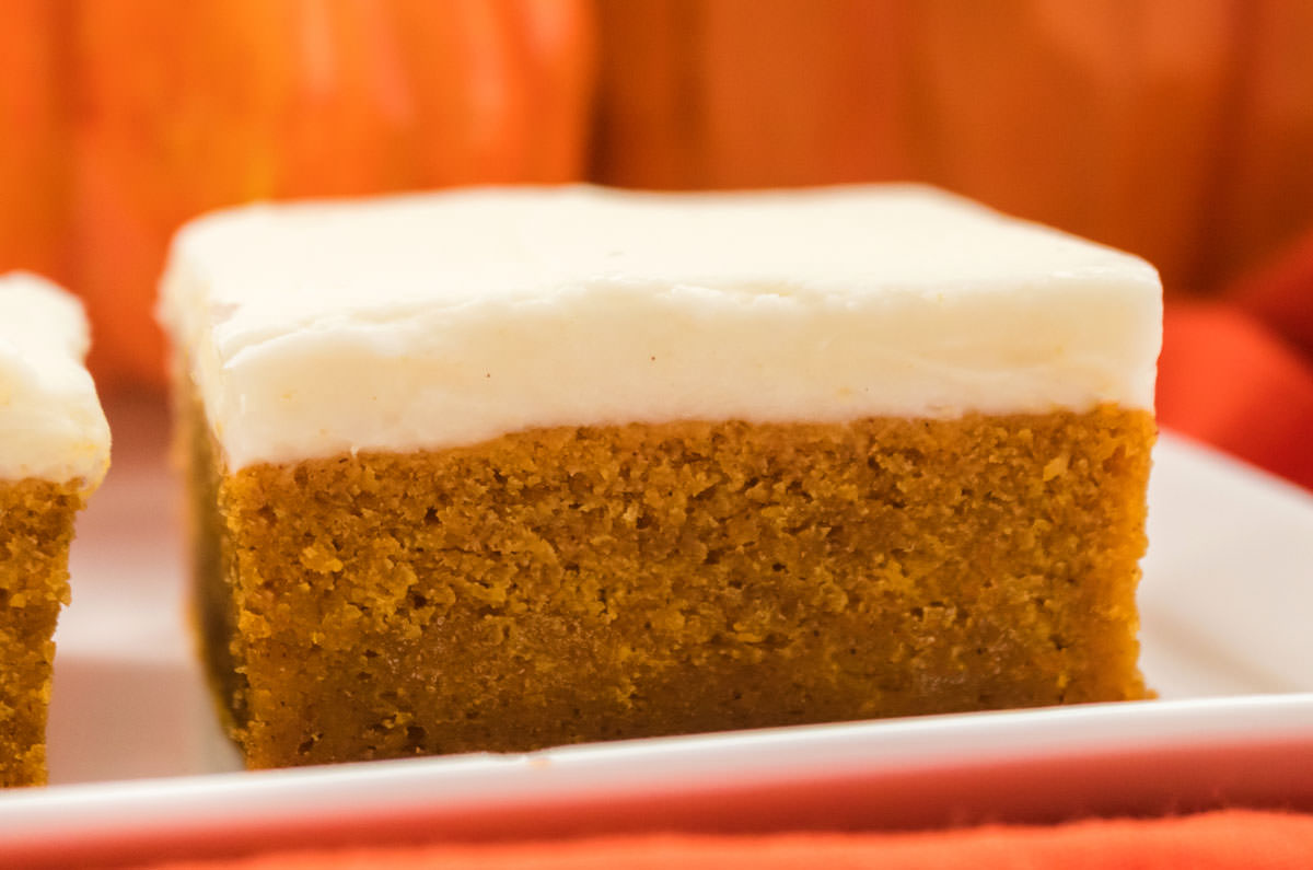 Closeup of a Pumpkin Bar with Cream Cheese Frosting sitting on a white serving platter in front of decorative pumpkins.