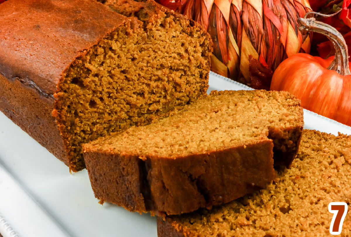 Closeup on a sideview of a loaf of sliced pumpkin bread sitting in front of fall pumpkins.