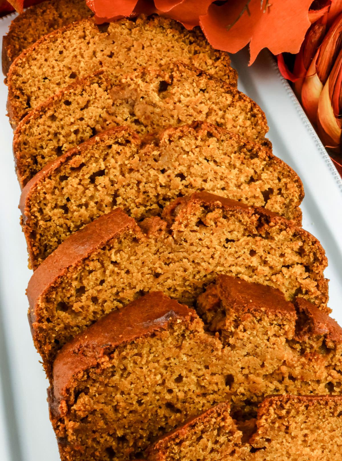Closeup on a long white serving platter holding seven slices of Homemade Pumpkin Bread.