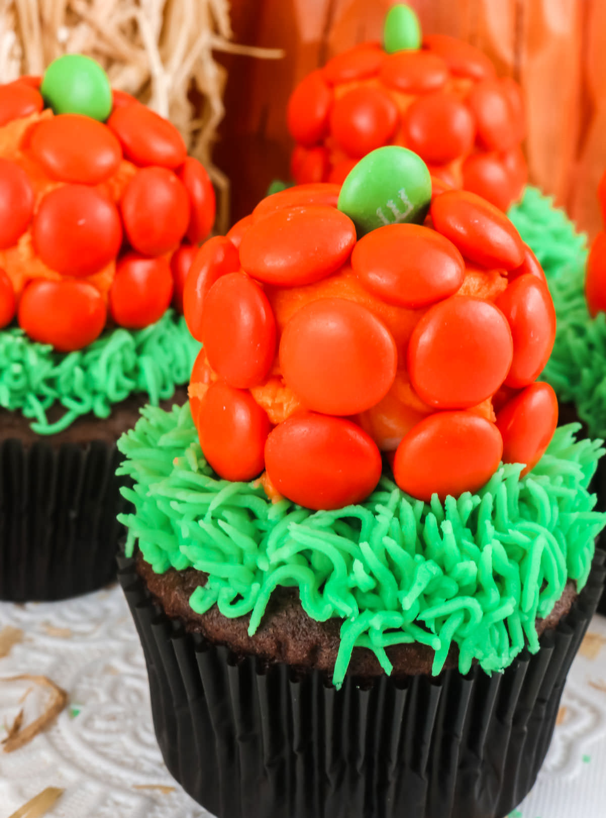 Closeup on three Pumpkin Patch Cupcakes sitting on a white table in front of Halloween Decorations.