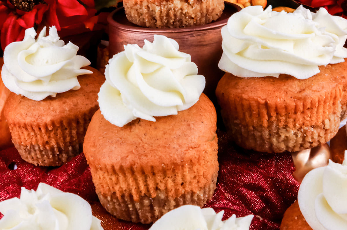 Three Pumpkin Pie Cupcakes sitting on a table filled with Autumn decorations.