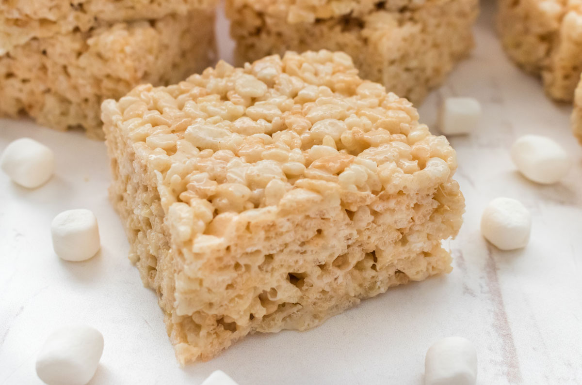 Closeup on a single Rice Krispie Treat sitting on a white surface surrounded by mini marshmallows.