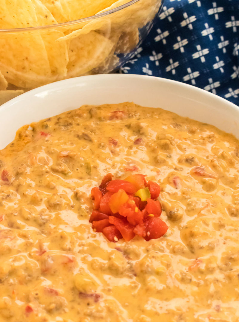 Rotel Dip in a white bowl with a spoonful of Ro-Tel Tomatoes in the center next to a glass bowl full of chips.