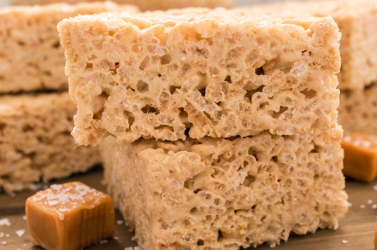 Closeup on a stack of two of The Best Salted Caramel Rice Krispie Treats sitting on a brown board next to caramel candies.