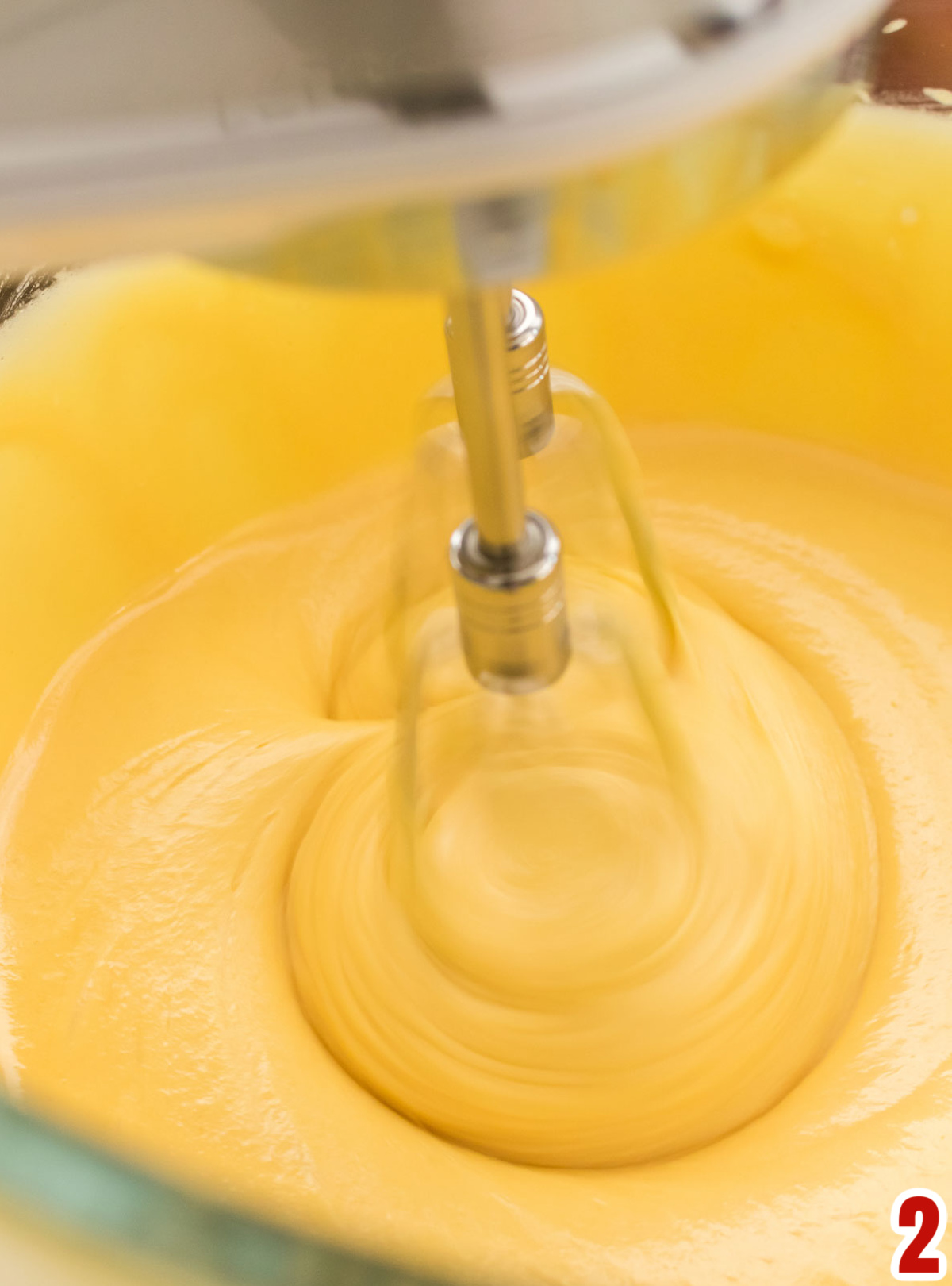 Closeup on glass mixing bowl with cake batter and a hand mixer.