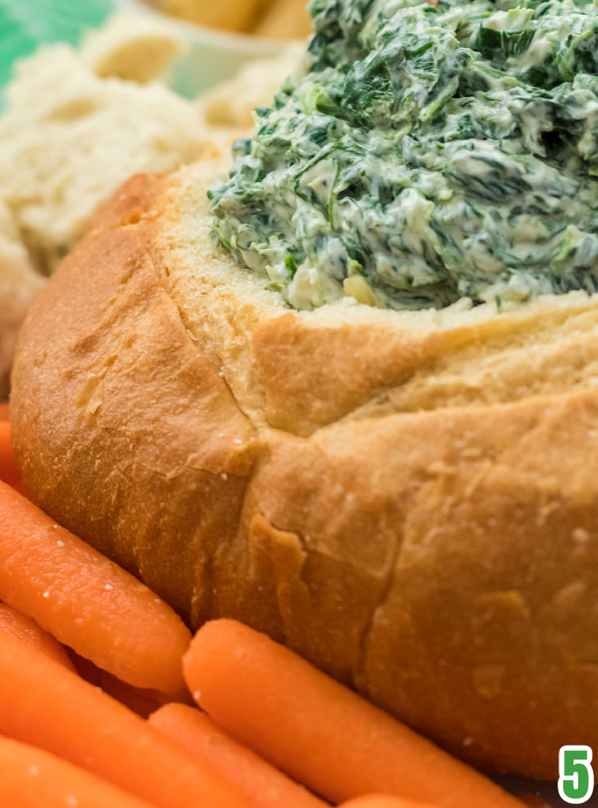 Closeup on a Sourdough round filled with Spinach Dip and surrounded by carrots and pieces of sourdough bread.