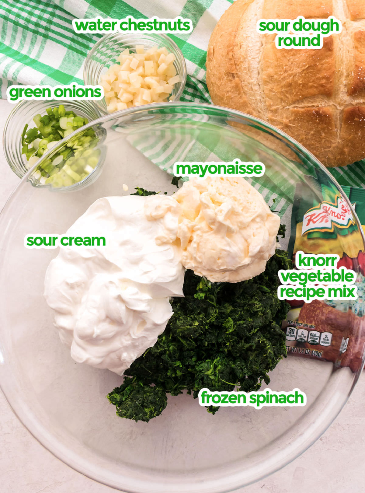 All the ingredients you will need to make Spinach Dip including frozen spinach, sour cream, mayonaisse, knorr vegetable recipe mix, green onions, watercress and a sourdough round.