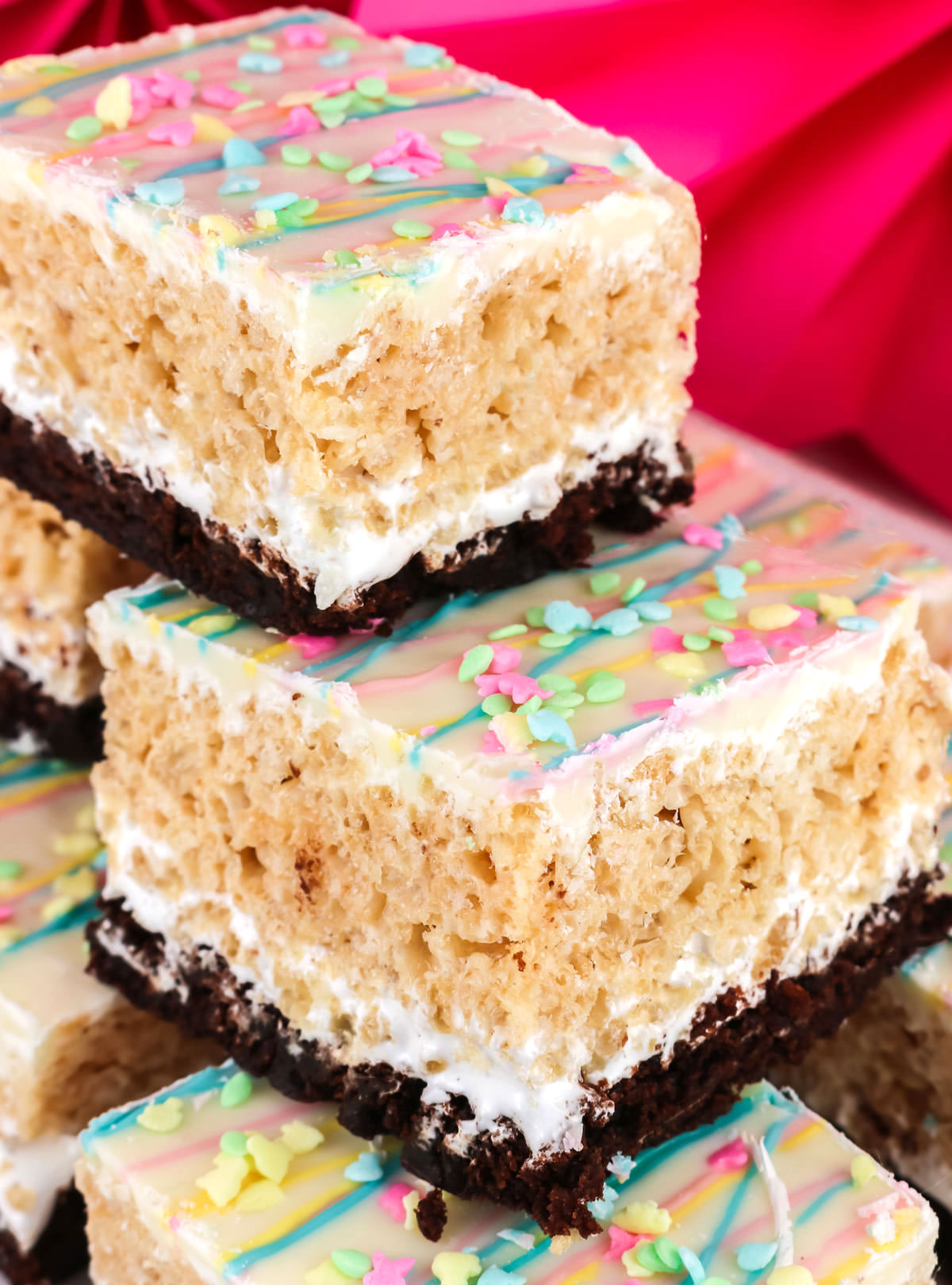 Closeup on a stack of Brownie Rice Krispie Treats in front of a pink background.