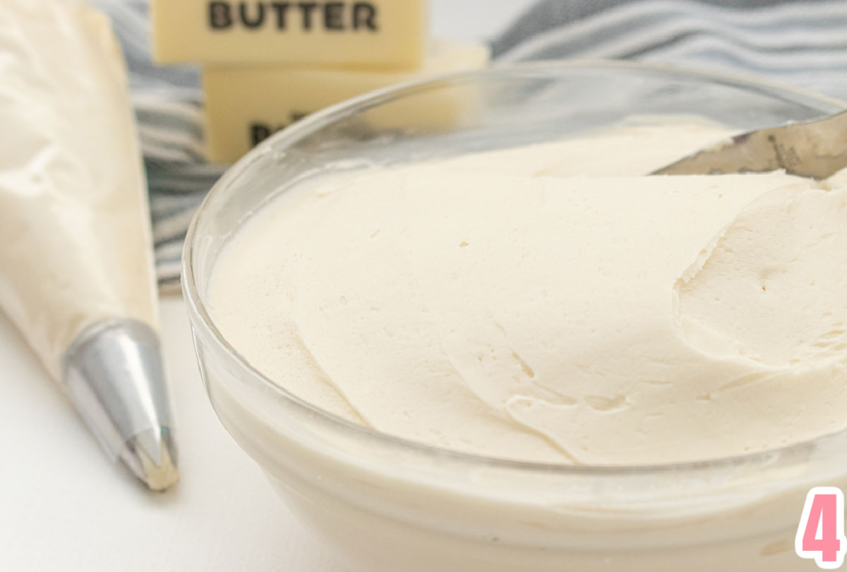 Close up of a glass bowl filled with The Best Buttercream Frosting sitting next to a decorating bag full of frosting.