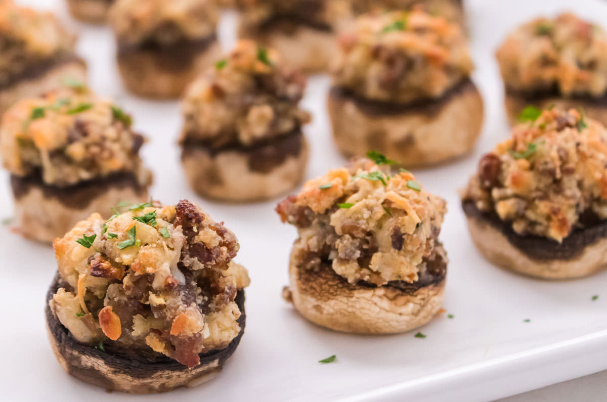 Closeup on a dozen Stuffed Mushrooms sitting on a baking sheet covered in parchment paper.