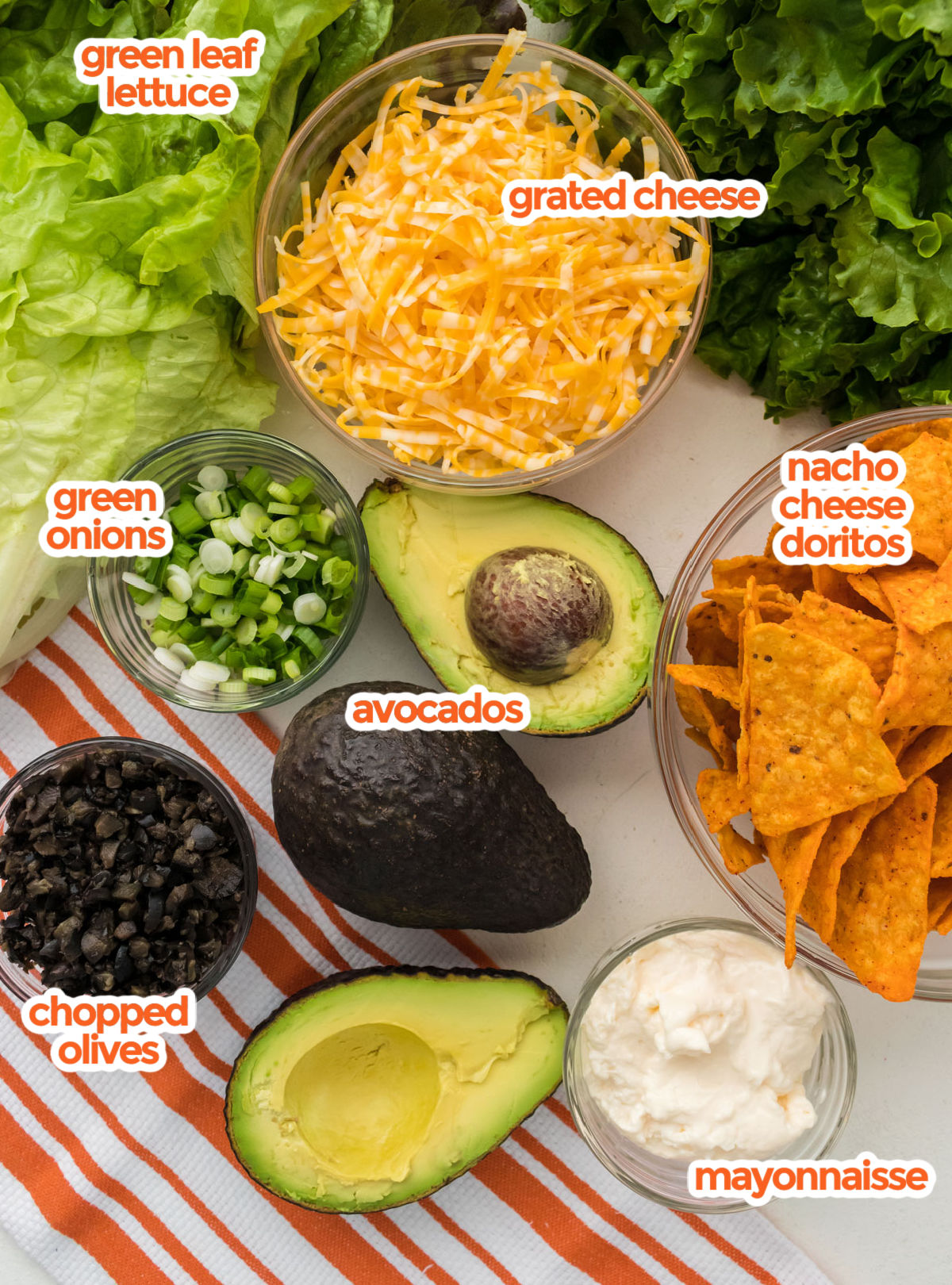 All the ingredients you will need to make Dorito Taco Salad including Green Leaf lettuce, Nacho Cheese Doritos, Avocados, Green Onions, Cheese, Chopped Olives and Mayonnaise.