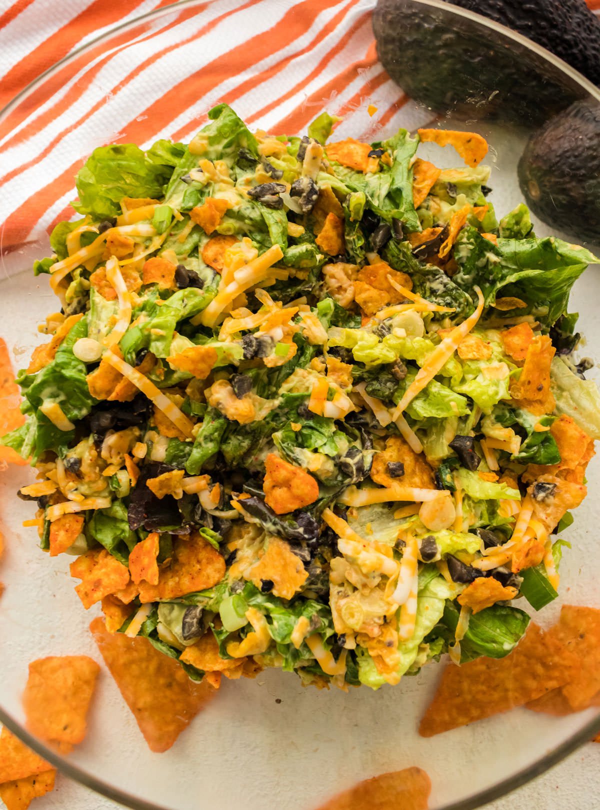 Closeup up of a glass bowl filled with Dorito Taco Salad surrounded by Nacho Cheese Doritos and Avocados.