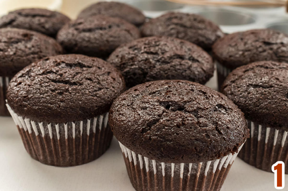 Closeup on ten chocolate cupcakes sitting on a white table.