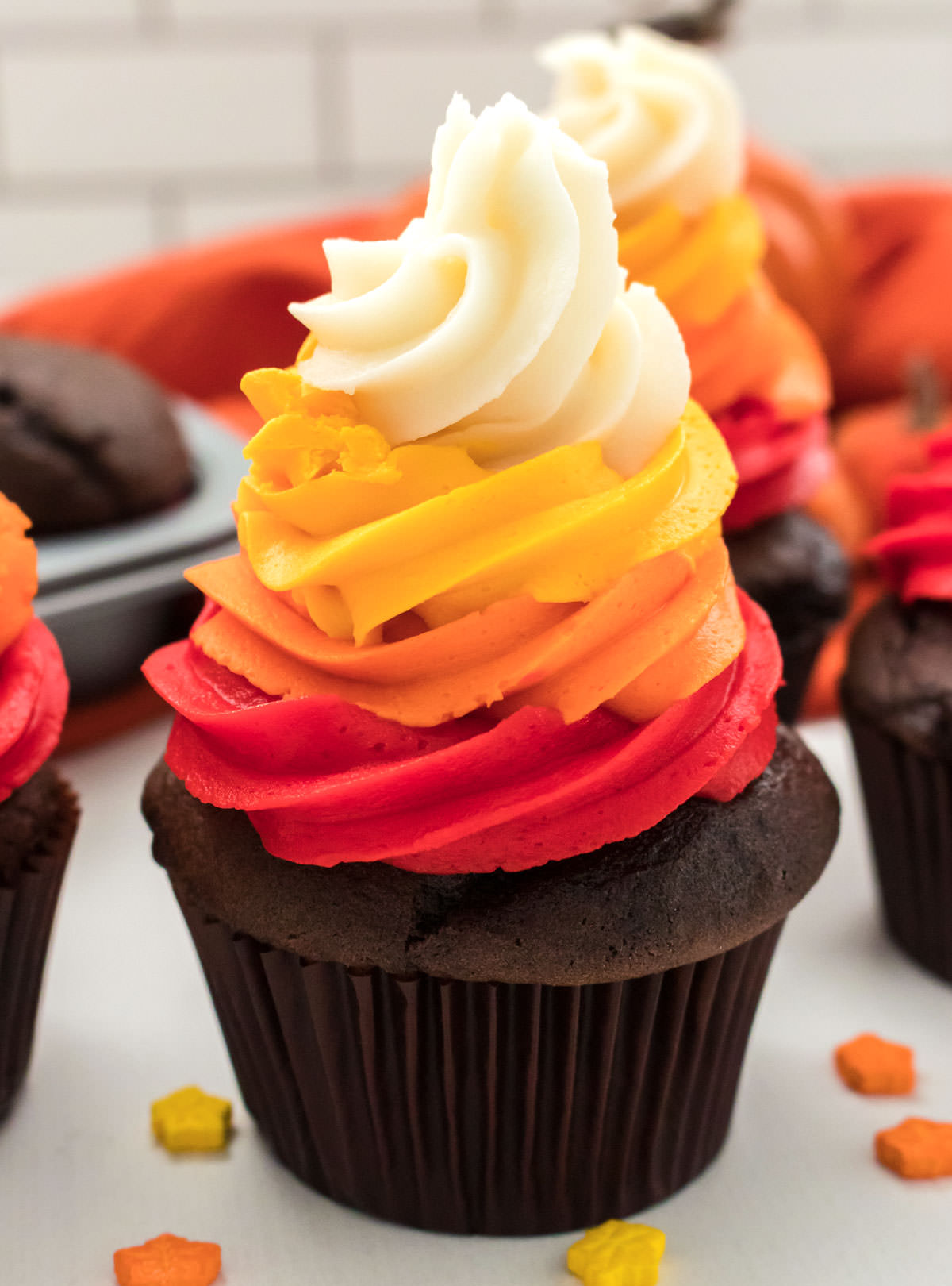 Closeup on a Harvest Thanksgiving Cupcake sitting on a white table in front of other cupcakes and surrounded by Thanksgiving sprinkles.