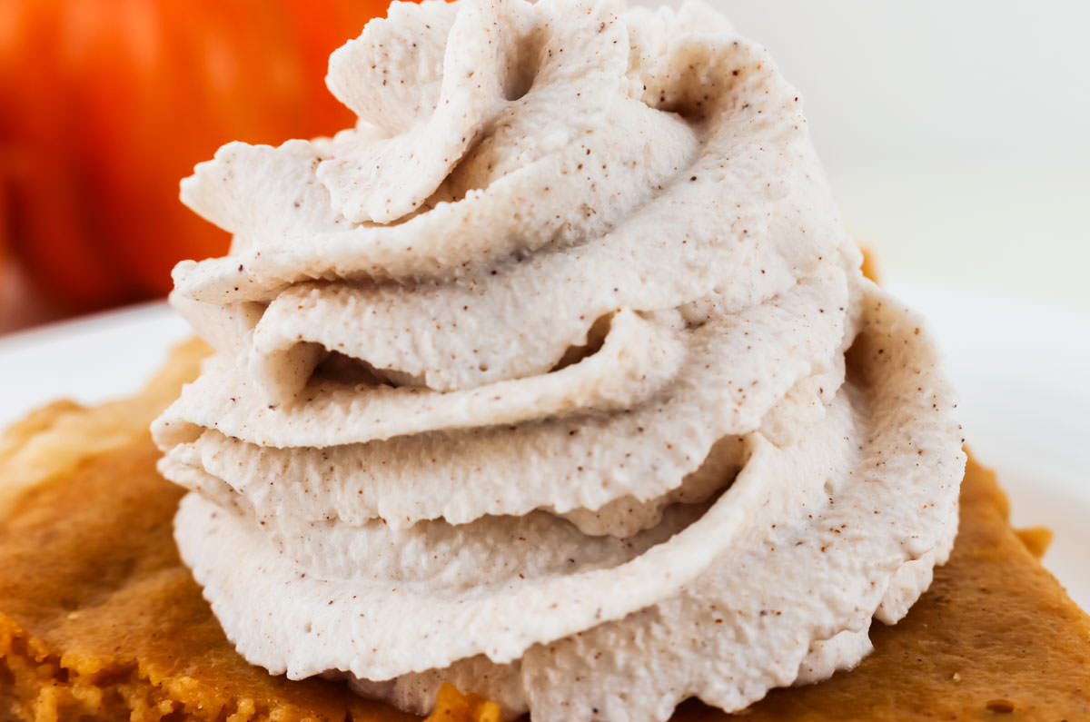 Closeup on a large swirl of Homemade Cinnamon Whipped Cream on top of a piece of Pumpkin Pie.