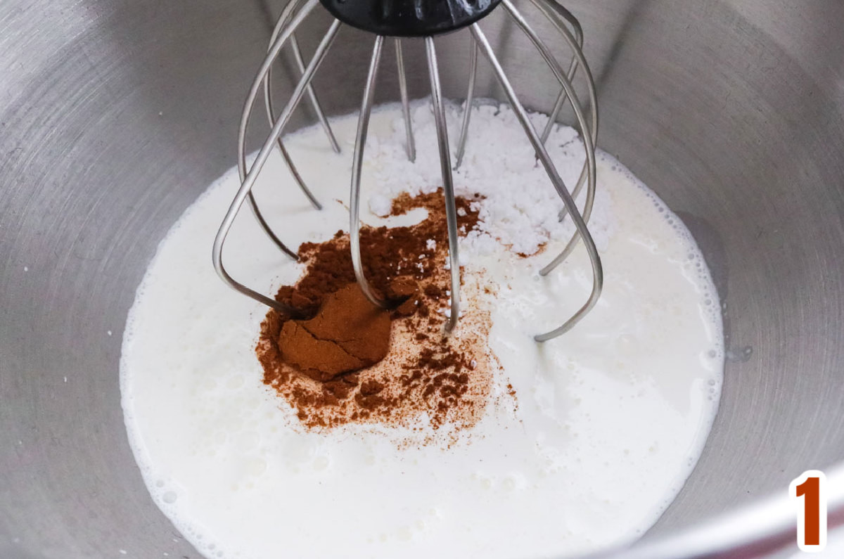 Closeup on a metal mixing bowl filled with Heavy Whipping Cream, Cinnamon and Powdered Sugar.