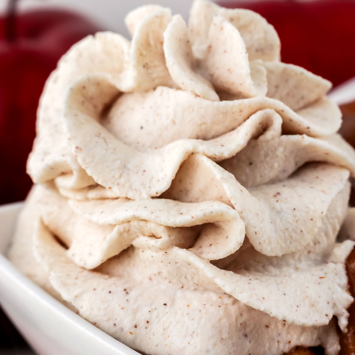 Closeup on a large swirl of Homemade Cinnamon Whipped Cream on a dessert in a white bowl.