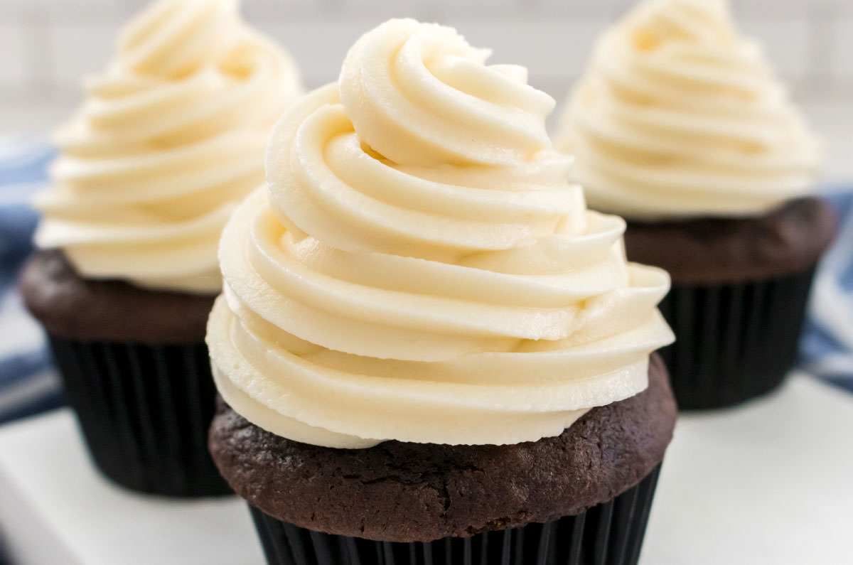Three chocolate cupcakes sitting on a white board frosted with swirls of The Best Cream Cheese Frosting.