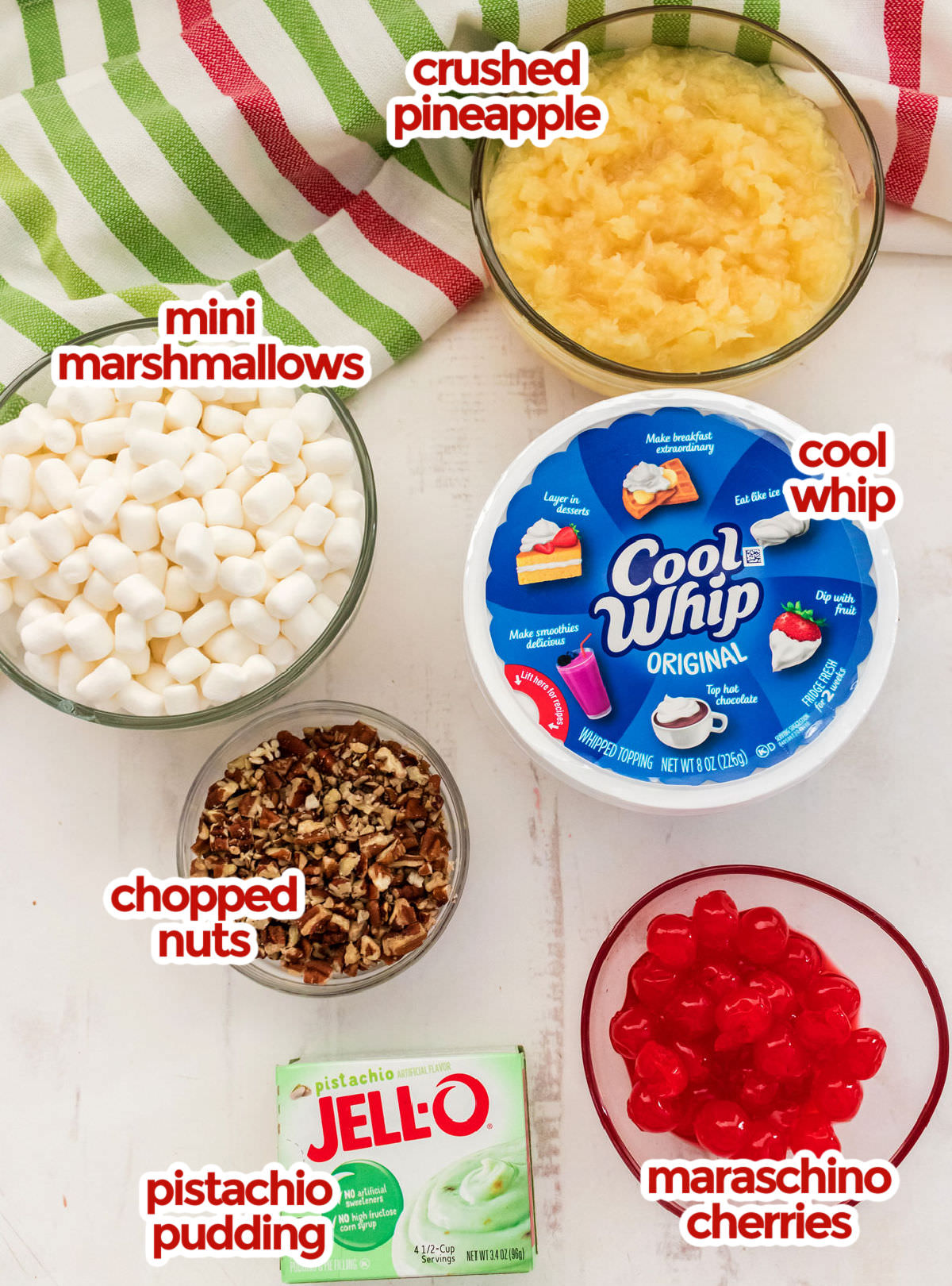 All the ingredients you will need to make Watergate Salad including Crushed Pineapple, Mini Marshmallows, Cool Whip, Chopped Nuts, Pistachio Instant Pudding and Maraschino Cherries.