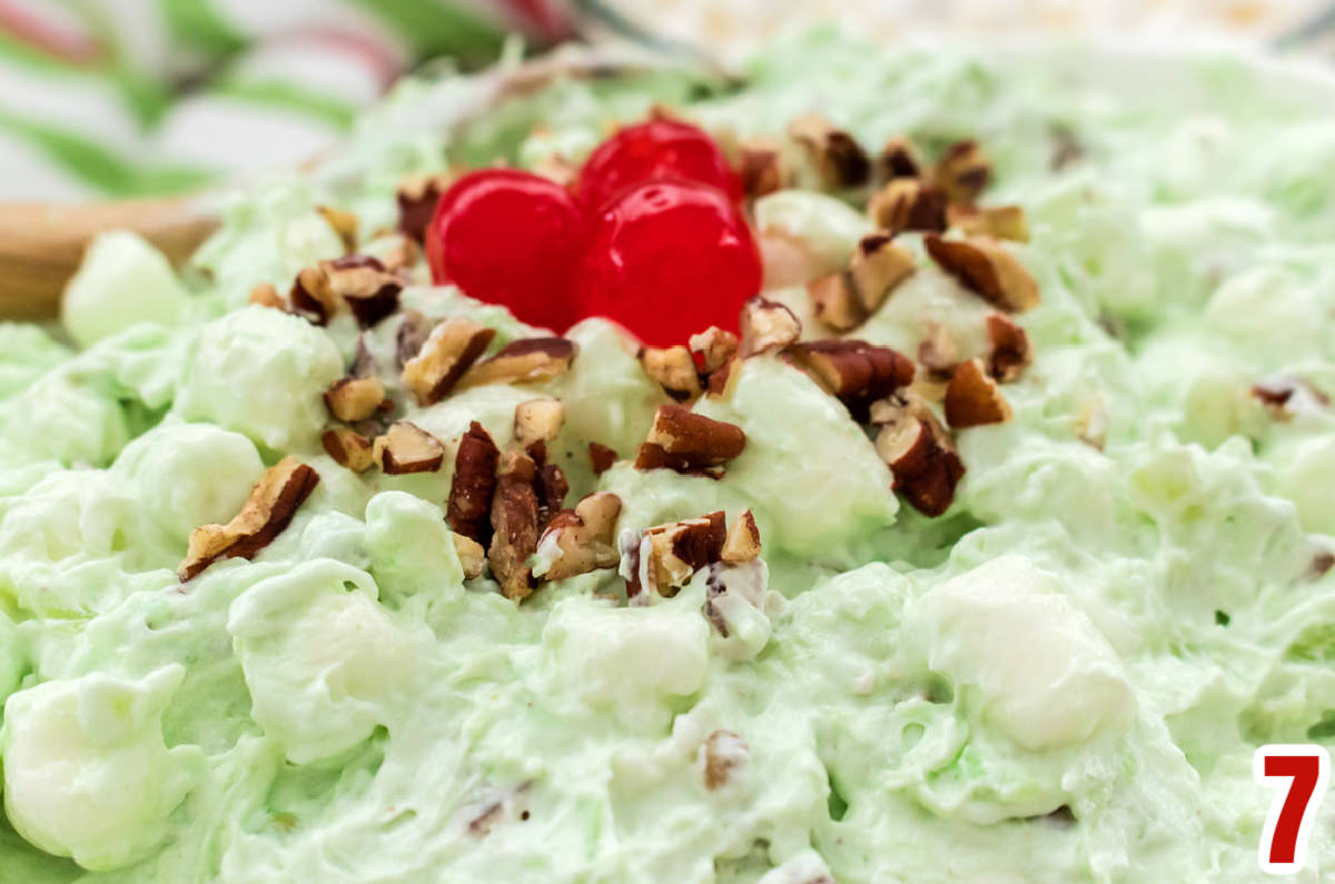 Closeup on a bowl of Watergate Salad or Pistachio Fluff topped with Maraschino Cherries and Chopped Nuts.