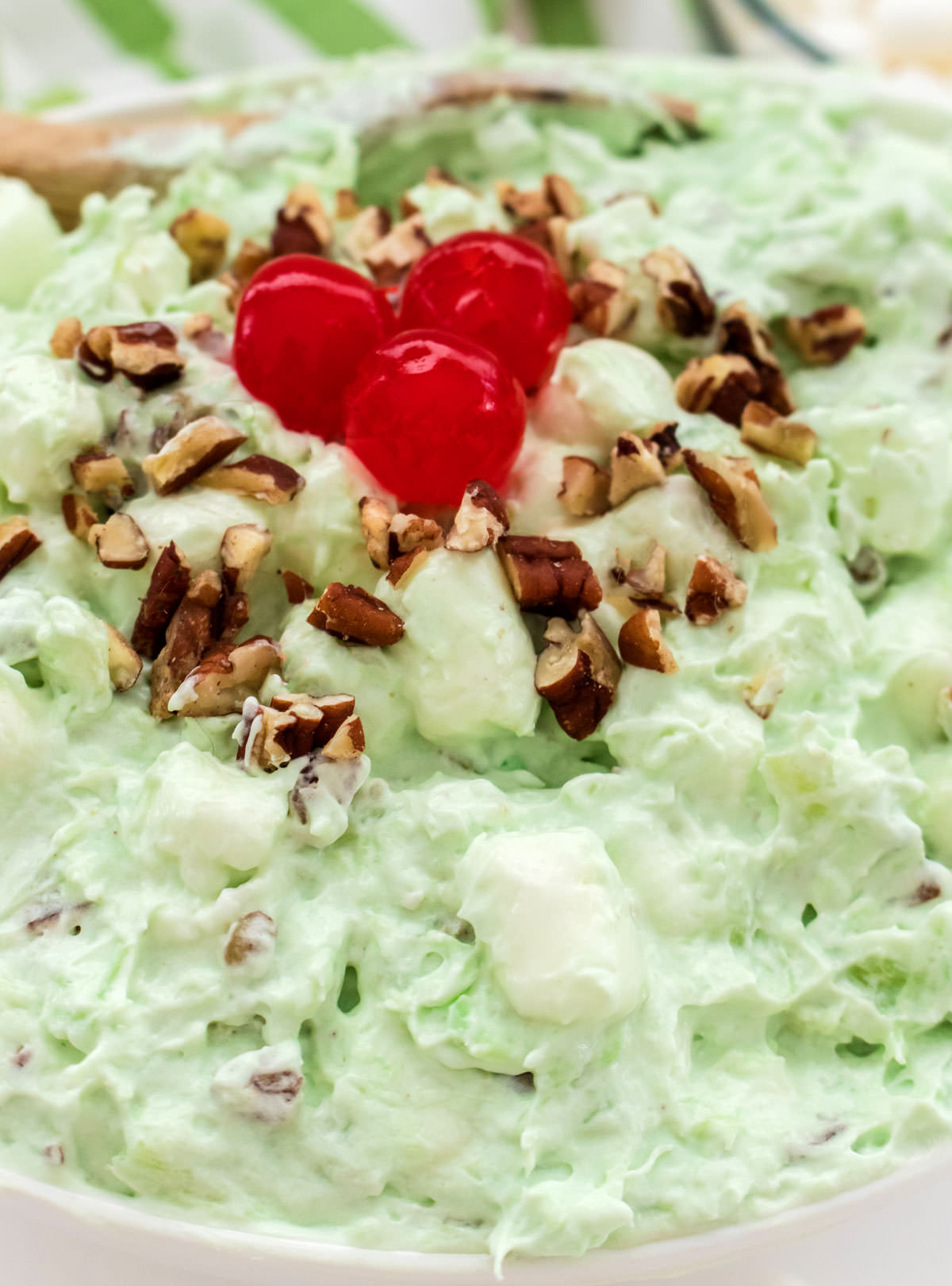 Closeup on a white serving bowl filled with Watergate Salad topped with chopped pecans and Maraschino Cherries.