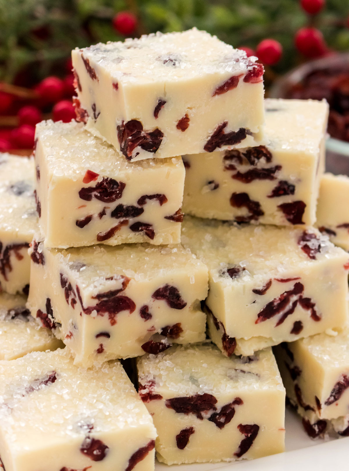 Close up on a stack of White Chocolate Cranberry Fudge sitting on a white serving platters in front of Christmas greenery.