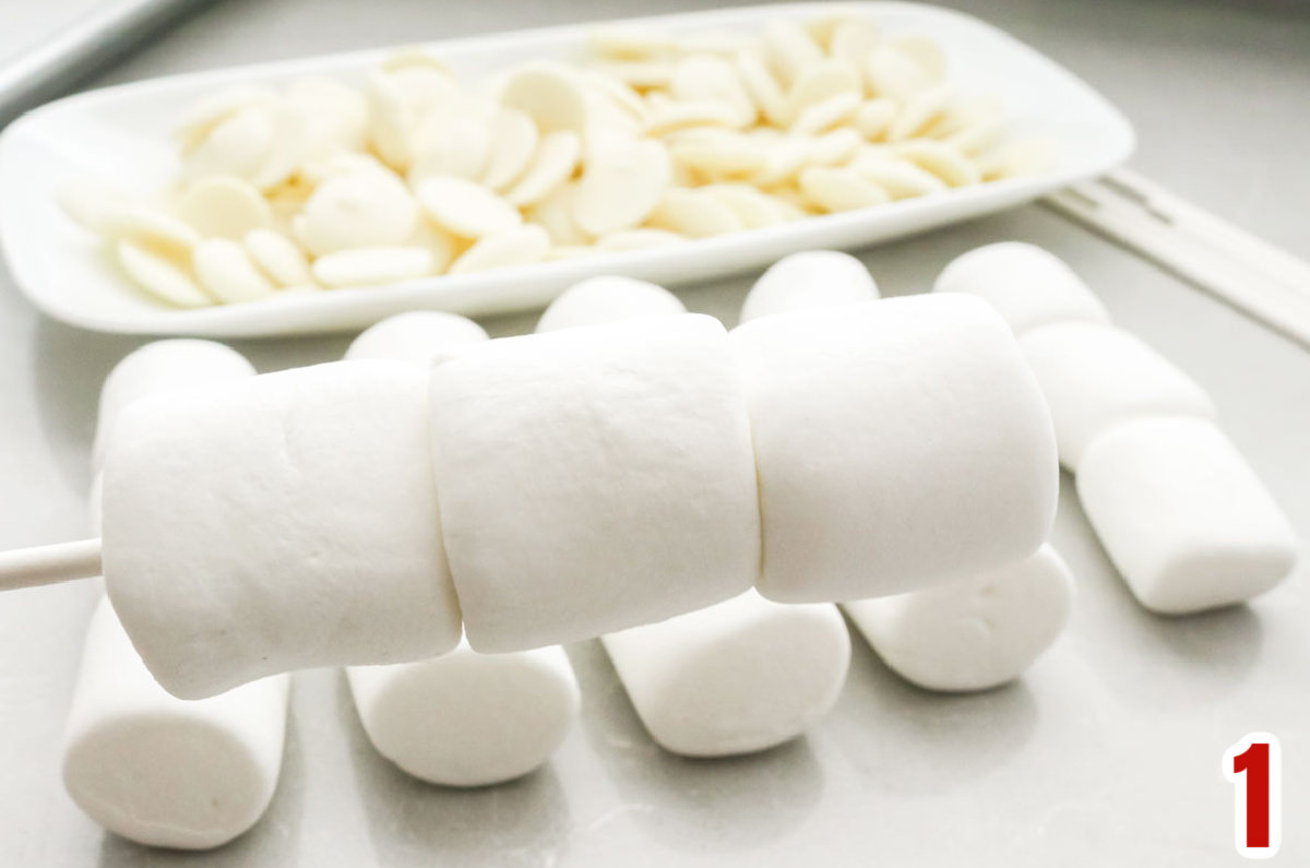 Closeup on a lollipop stick holding three regular marshmallows.